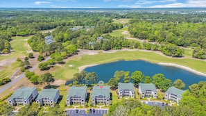Vista aérea de um campo de golfe com um lago, rodeado por vegetação exuberante e edifícios residenciais.