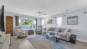 A living room with a flat-screen TV, two recliner chairs, a sofa, a coffee table, and a large window with a view.