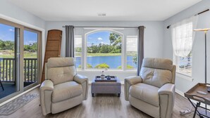 A room with two leather armchairs, a small ottoman, and a view of a lake through large windows.