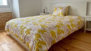 Ein Schlafzimmer mit Bett, Holzboden, weißen Wänden, einem Nachttisch und einem Fenster.