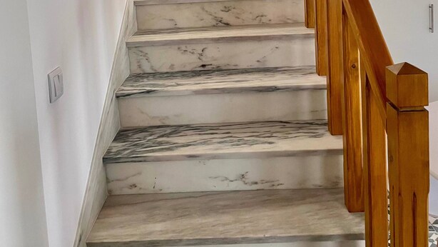Eine Marmortreppe mit hölzernen Geländern, die zu einer Zwischenebene führt.