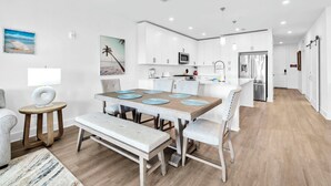 Una cocina moderna con armarios blancos, un refrigerador de acero inoxidable y un comedor con una mesa de madera y bancos.