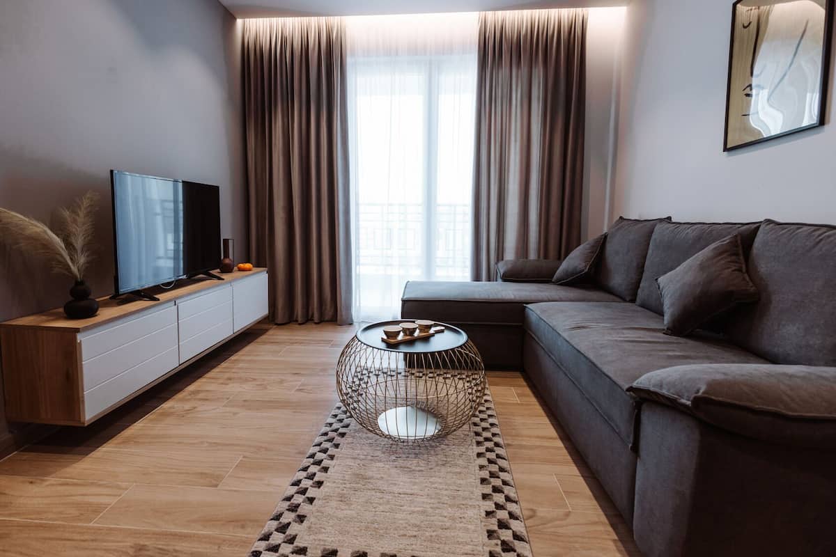 Un salon moderne avec un canapé, une table basse, un téléviseur posé sur un meuble et une grande fenêtre avec des rideaux.