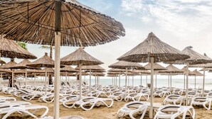 A beach with rows of white lounge chairs and thatched umbrellas. - Bonita Luxury Resort & Spa (Golem)