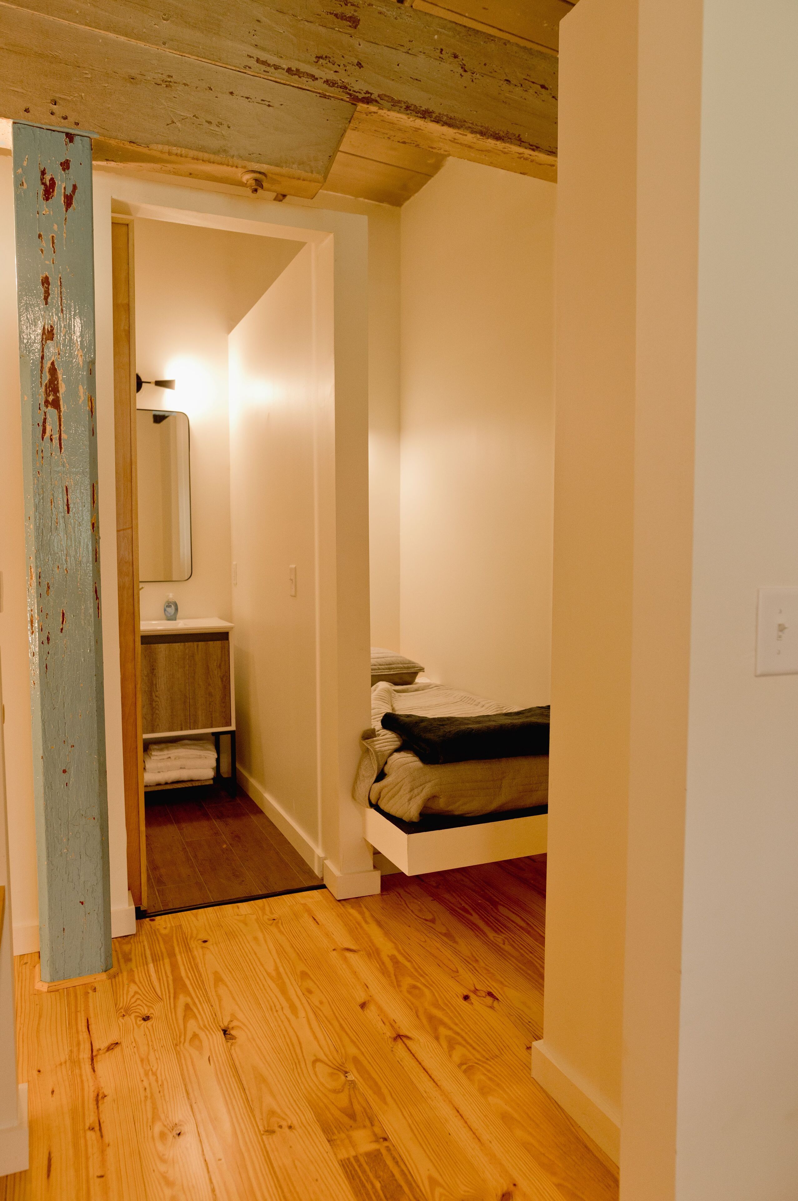 A narrow hallway with wooden flooring leading to a bathroom with a sink and a mirror.