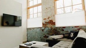 Un salón con pared de ladrillo, un sofá blanco, una mesa de centro y un televisor montado en la pared.