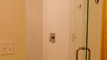 A glass-enclosed shower with white tiles, a visible electrical outlet, and a toilet paper holder on the wall.