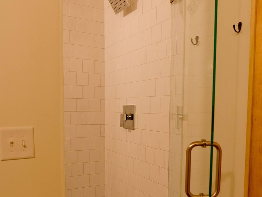 A glass-enclosed shower with white tiles, a visible electrical outlet, and a toilet paper holder on the wall.