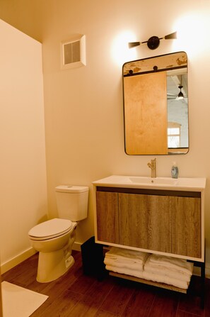 A bathroom with a white toilet, a wooden vanity with a mirror, and a towel rack. - Loom Room Retreat (Dalton)