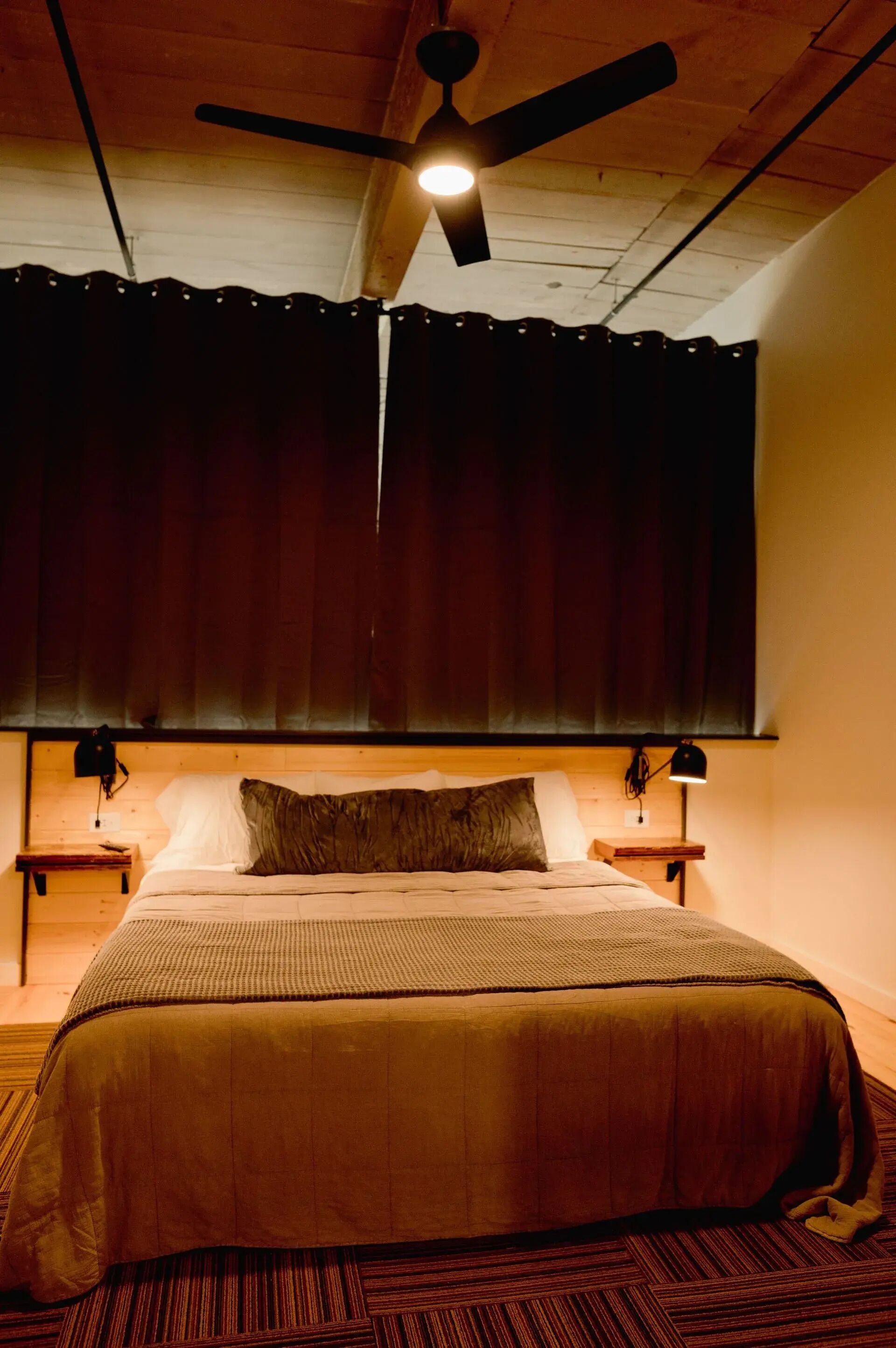 A bedroom with a bed, a ceiling fan, a window with curtains, and bedside lamps.