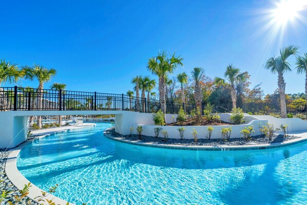 A swimming pool with a curved design, surrounded by palm trees and a white fence.