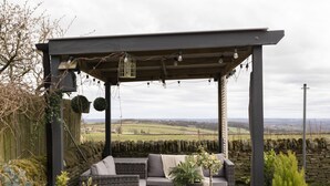 Een overdekt terras met een pad van stenen, omringd door een tuin met verschillende planten en bloemen.