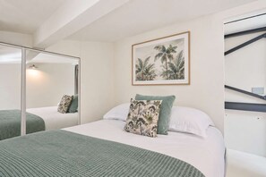 A bedroom with a bed, a mirror, a framed botanical print, and a staircase.