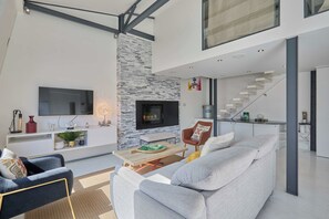 Ein modernes Wohnzimmer mit einer Wand aus Stein, einem Flachbildfernseher, einem Kamin und einer Treppe, die zu einer oberen Ebene führt.