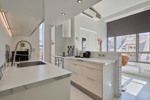 A modern kitchen with a central island, built-in appliances, and a large window providing a view of the cityscape.