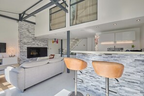 A modern living room with a stone accent wall, a fireplace, a sofa, and two bar stools.