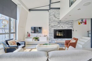 Ein modernes Wohnzimmer mit Kamin, Flachbildfernseher und großem Fenster.