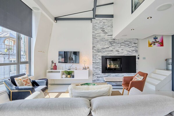 A modern living room with a fireplace, a flat-screen TV, and a large window.