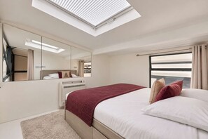 Ein Hotelzimmer mit Oberlicht, einem großen Bett, einem Spiegel und Meerblick.