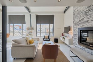 A modern living room with a sofa, coffee table, and a flat-screen TV mounted on a stone wall.