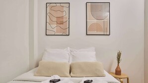 A neatly made bed with white linens and two beige pillows, a small wooden side table with a vase of flowers, and two abstract art pieces on the wall. - Magnificent flat in Saint Germain des Près (Paris)