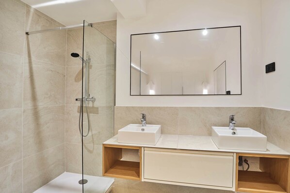 A modern bathroom with a glass-enclosed shower, two sinks, and a large mirror.