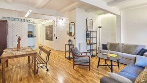A spacious living room with a wooden floor, a sofa, a coffee table, a dining table with placemats, and a fireplace. - Magnificent flat in Saint Germain des Près (Paris)