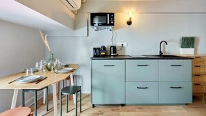 A compact kitchen with a microwave, coffee maker, and sink. There is a dining table with chairs and a vase of dried plants. - Charming Studio Center of Paris with AC (Paris)
