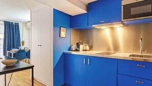 A modern kitchen with blue cabinets, a stainless steel range hood, and a dining area with a table and chairs. - Sublime apartment Le Marais / Beaubourg (Paris)
