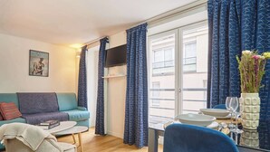 A living room with a sofa, a dining table with chairs, a TV, and a window with curtains. - Sublime apartment Le Marais / Beaubourg (Paris)