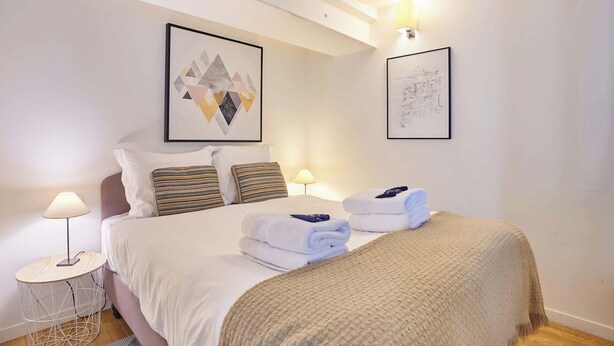 A hotel room with a bed, two bedside tables, a lamp, and two framed artworks on the walls. - Sublime apartment Le Marais / Beaubourg (Paris)