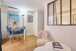 Un comedor con una mesa dispuesta para cuatro personas, una silla azul, una silla blanca y un libro sobre una mesita.