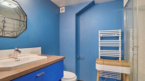 A bathroom with a blue wall, a white sink, a toilet, and a shower area. - Sublime apartment Le Marais / Beaubourg (Paris)