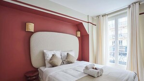 A hotel room with a large bed, a red accent wall, and a view of the city through a balcony. - Sublim & NEW apartement St Germain/Notre Dame (Paris)