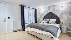 A modern bedroom with a large bed, a radiator, a window with curtains, and a wall-mounted light fixture. - New apartment Centre de Paris Bourse (Paris)
