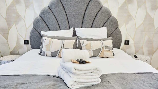 A neatly made bed with a grey upholstered headboard, white bedding, and a stack of white towels. - New apartment Centre de Paris Bourse (Paris)