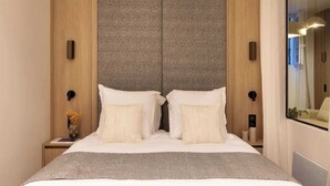A modern hotel room with a large bed, a wooden wardrobe, and a nightstand with a vase of flowers.