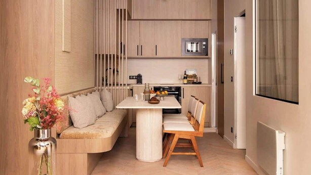 A modern kitchen with a built-in microwave, a dining area with a white table and wooden chairs, and a kitchen island with a sink.