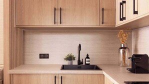 A modern kitchen with light wood cabinetry, a black sink, and a built-in oven.