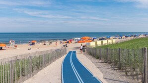 Ein Strand mit blauer Laufbahn, Sonnenschirmen und Menschen.