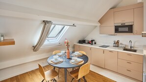 Eine moderne Küche mit Backofen, ein Essbereich mit rundem Tisch und Stühlen sowie ein Fenster mit Vorhängen.