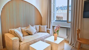 Un salon moderne avec un canapé, deux tables d’appoint, un vase décoratif et une vue sur les immeubles par la fenêtre.