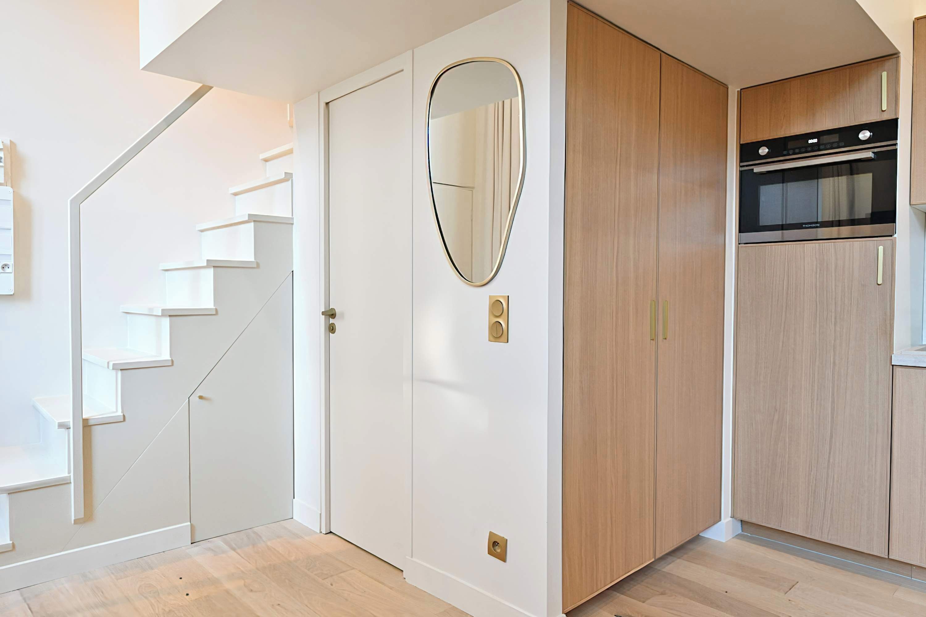 A modern kitchen with wooden cabinets, a built-in oven, and a white door with a mirror.