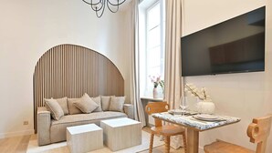 Un salon moderne avec un canapé, une table basse et une table à manger avec des chaises. Un téléviseur à écran plat est fixé au mur.