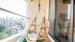 A wicker swing chair on a balcony with a city view.