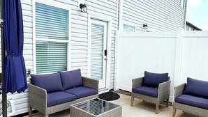Un patio con mobiliario de mimbre y una mesa de centro de vidrio.