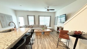 Una cocina moderna con encimera de granito, zona de comedor con mesa de madera, sofá y escalera.