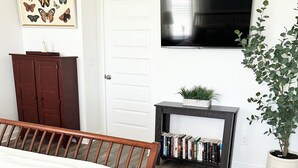 Un dormitorio con cama, televisor montado en la pared, estantería y planta en maceta.