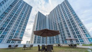 A modern high-rise building with multiple floors, large windows, and a grassy outdoor area with tables and chairs. - Free Wifi and Netflix | The Linear Makati CRQ-1 (Makati)