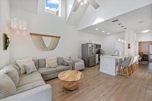 Uma sala de estar espaçosa com sofá, mesa de centro de madeira e cozinha equipada com geladeira e micro-ondas.